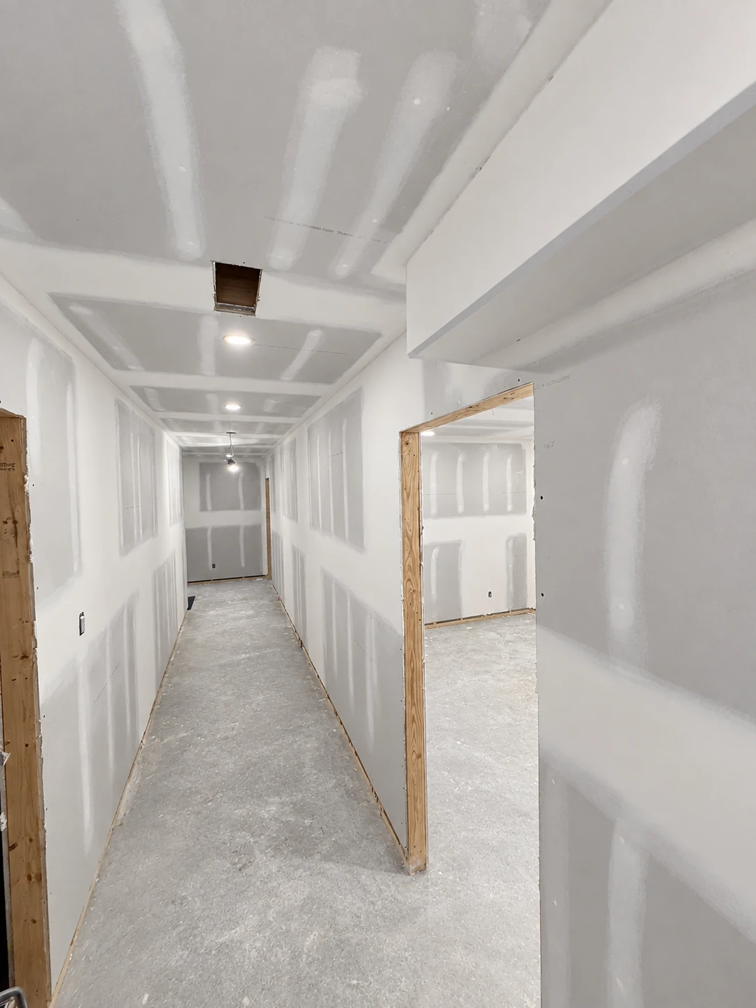Basement hallway with taped drywall joints, an unfinished doorway and ceiling bulkheads.